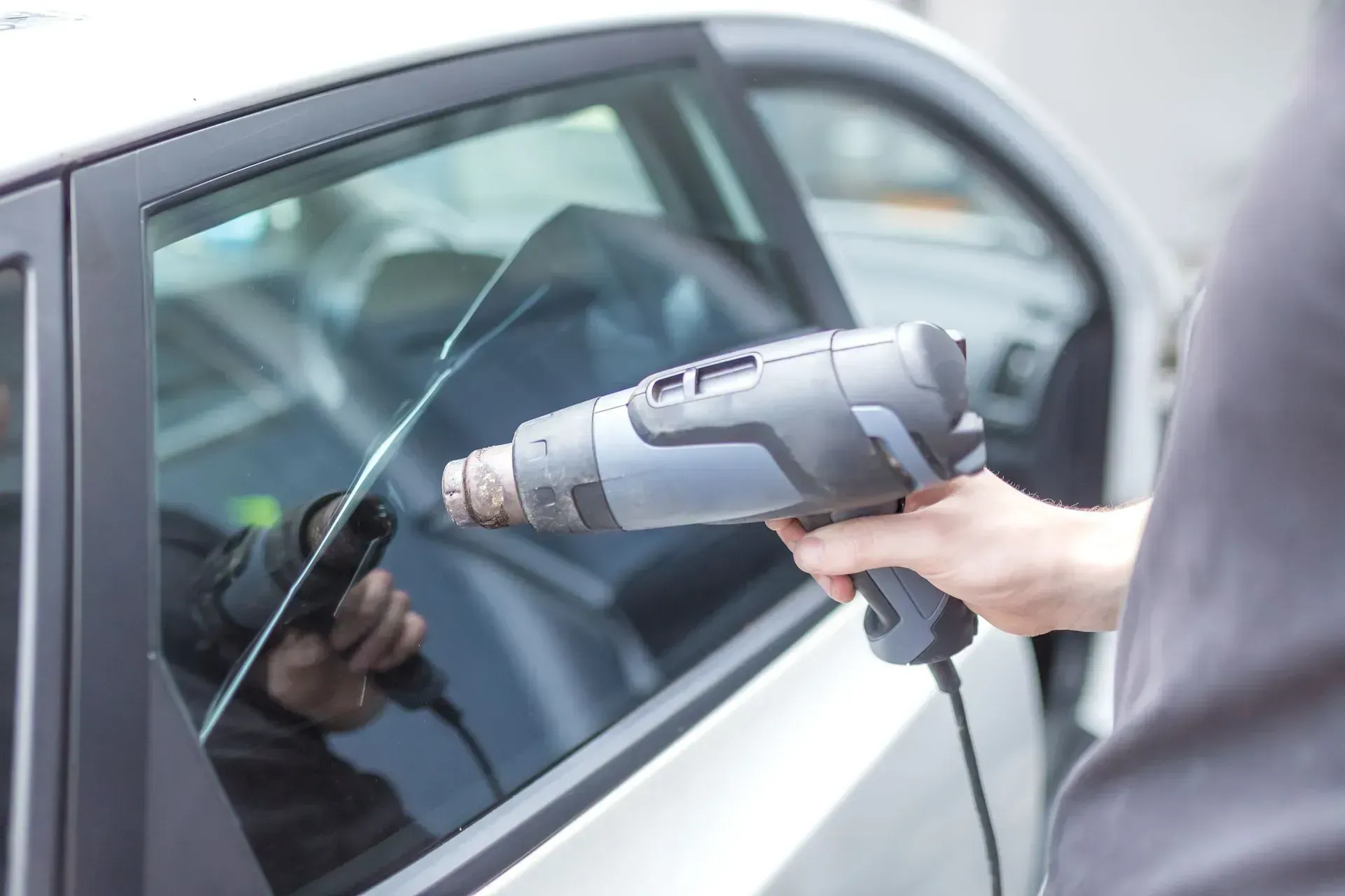 A person using a heat gun to apply tint film to a car window.