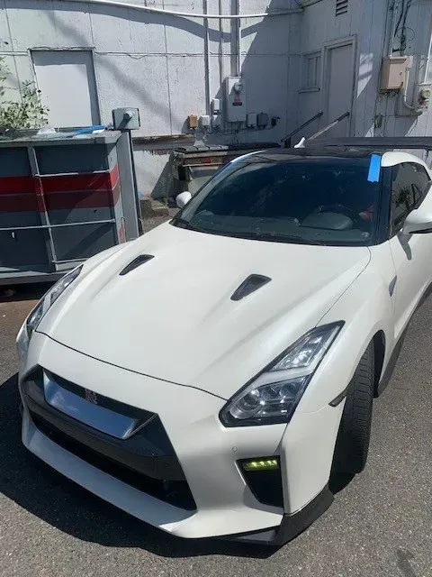 A white Nissan GT-R parked outdoors on a paved surface next to a grey metal utility structure.