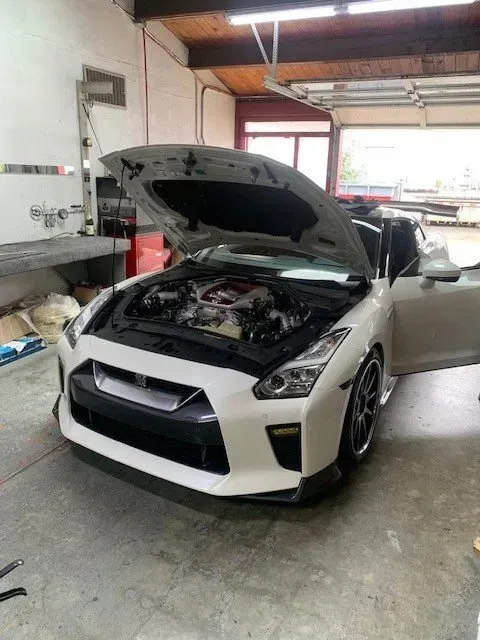 A white Nissan GT-R sports car with its hood open in a garage workshop.