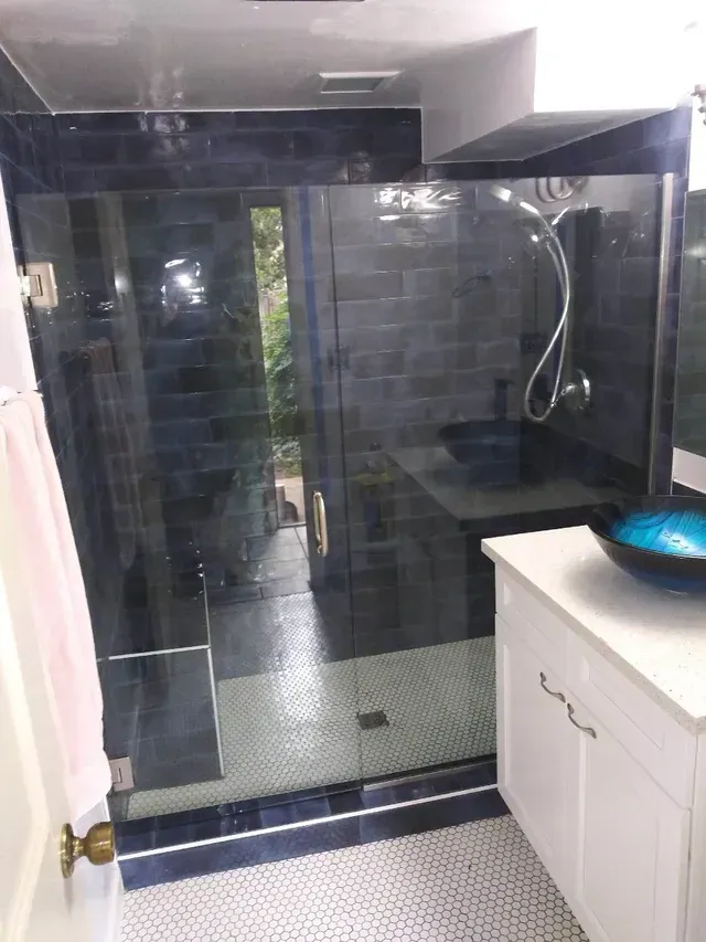 Modern bathroom featuring a glass shower stall with dark blue tiles, a white vanity, and a blue bowl sink on a tiled floor.