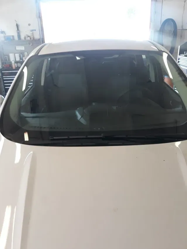 A close-up, high-angle view of a white car hood leading to the windshield and interior, set in a garage.