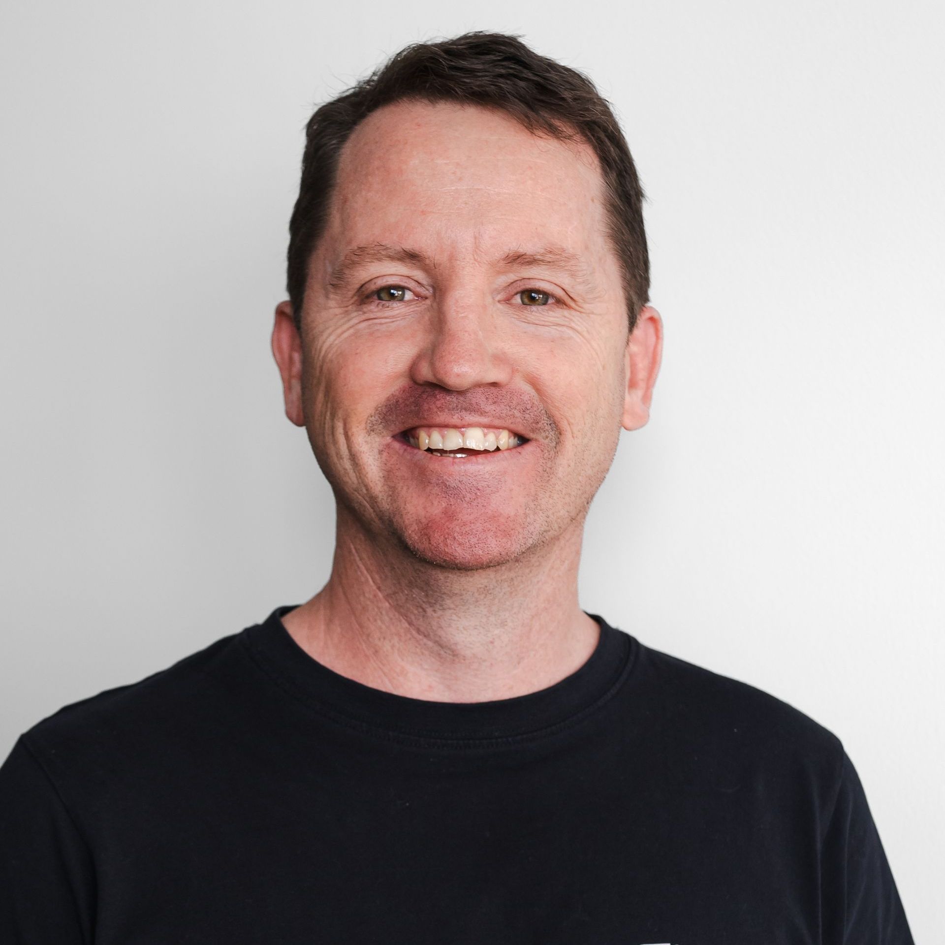 Greg Dwan wearing a black shirt is smiling for the camera.