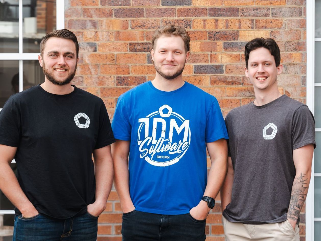 David, Ethan and Wade are standing in front of a brick wall and one of them is wearing a blue shirt that says JDM software