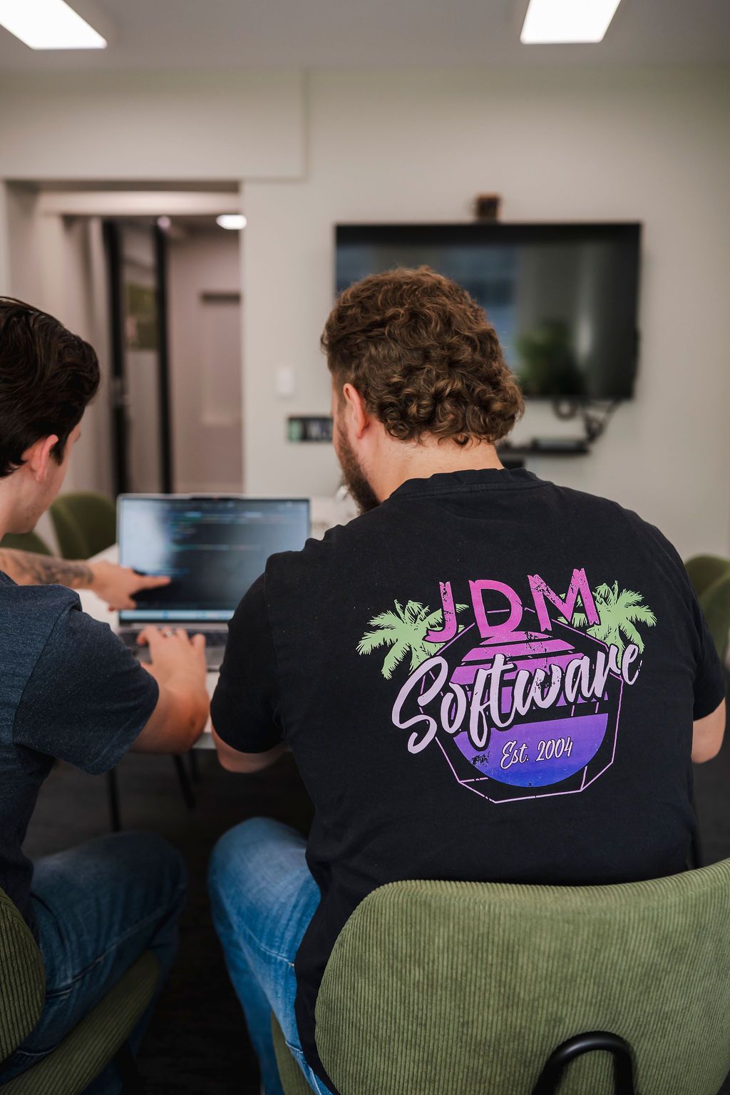 Two men are looking at a laptop computer in front of a window.