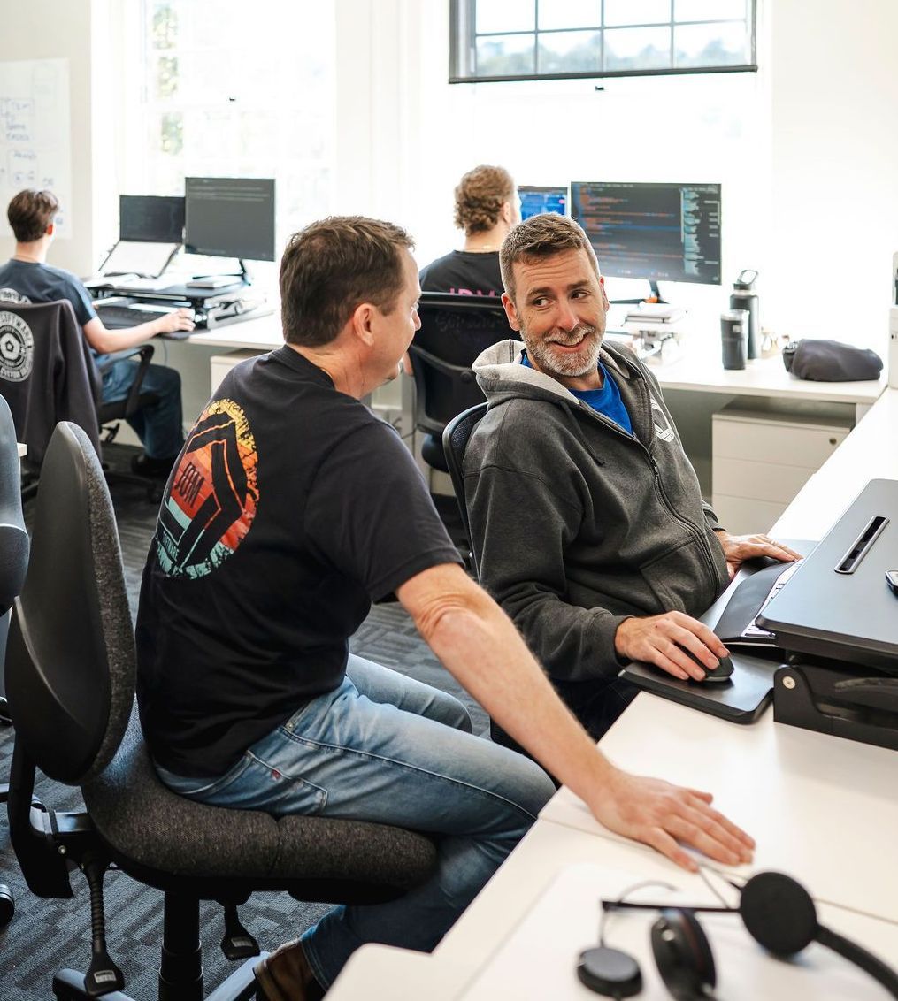 Two men are sitting at a desk looking at a computer screen.