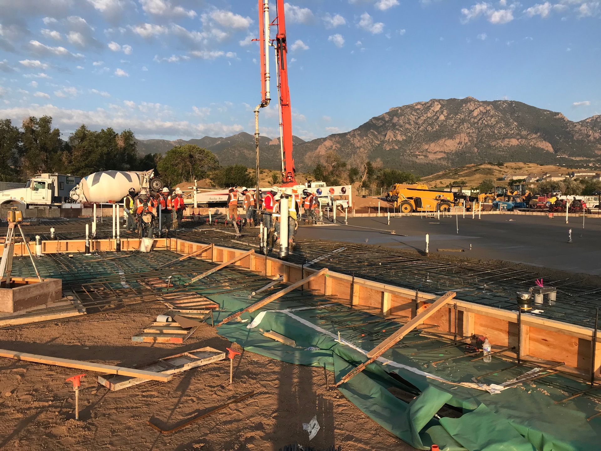 A concrete pump is being used to pour concrete on a construction site with mountains in the background.