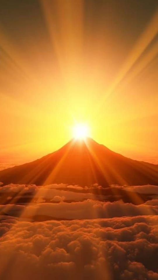 Ein Sonnenuntergang über einem Berg, bei dem die Sonne durch die Wolken scheint.