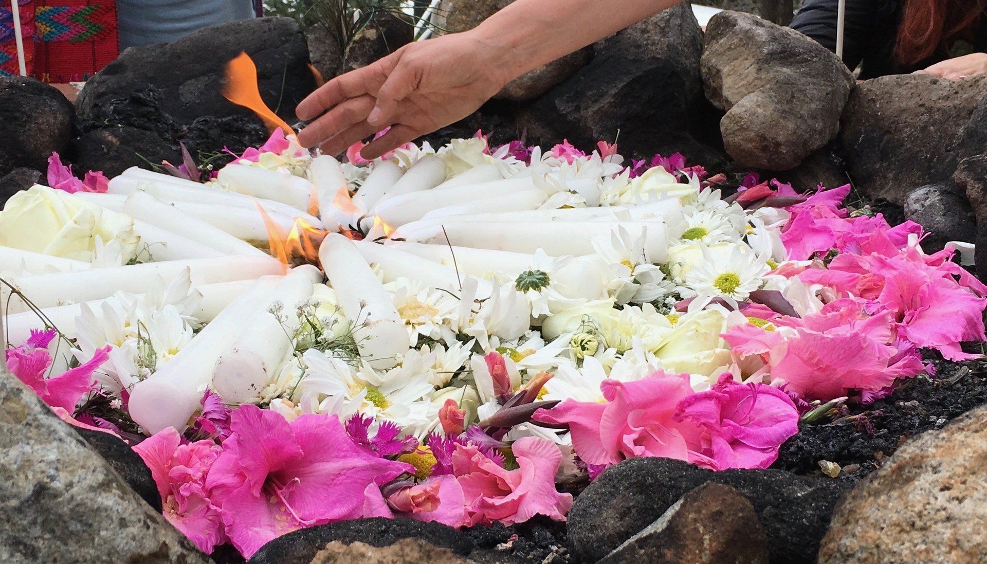 Eine Person zündet in einem Blumenkreis eine Kerze an.