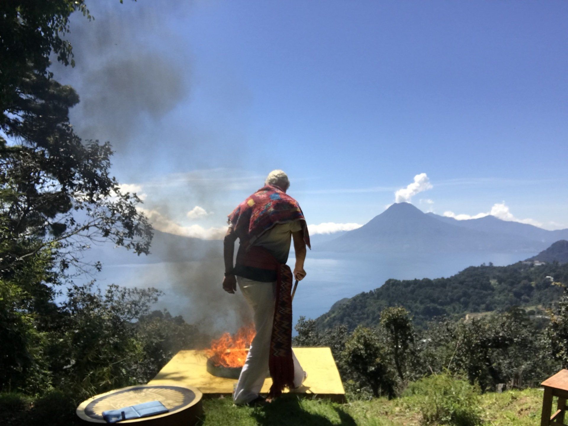 Ein Mann steht vor einem Feuer, im Hintergrund ist ein Berg zu sehen.