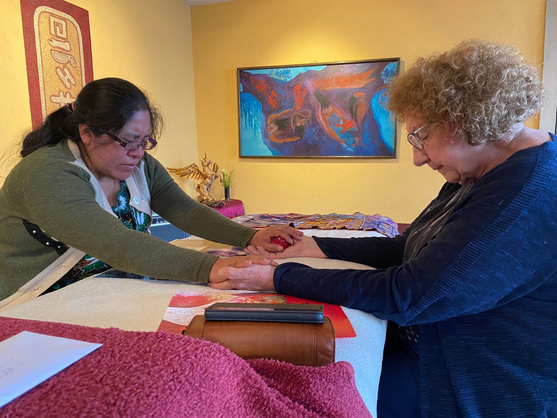 Zwei Frauen sitzen mit gefalteten Händen an einem Tisch.