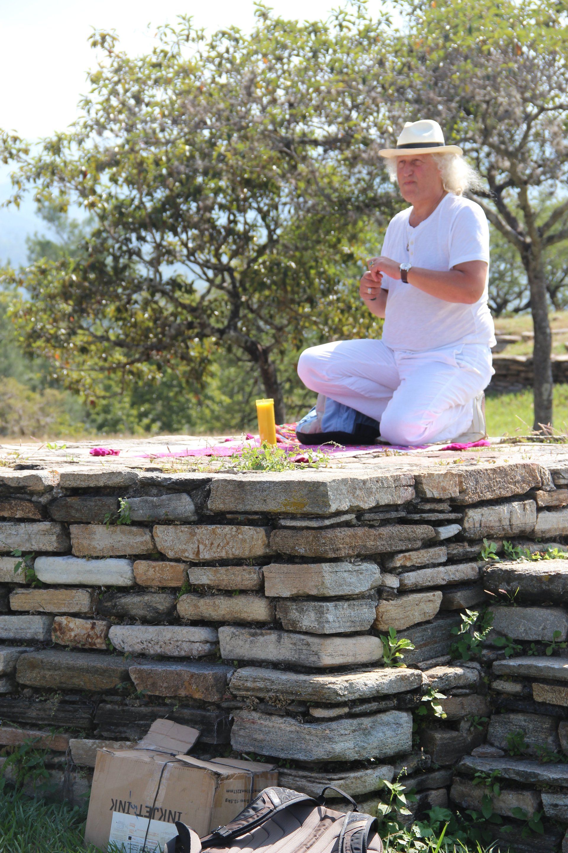 Ein Mann in weißem Hemd und Hut kniet auf einer Steinmauer.