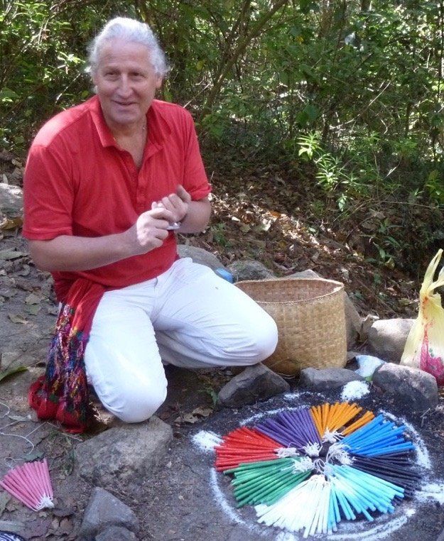 Ein Mann in einem roten Hemd kniet vor einem Kreis aus Räucherstäbchen