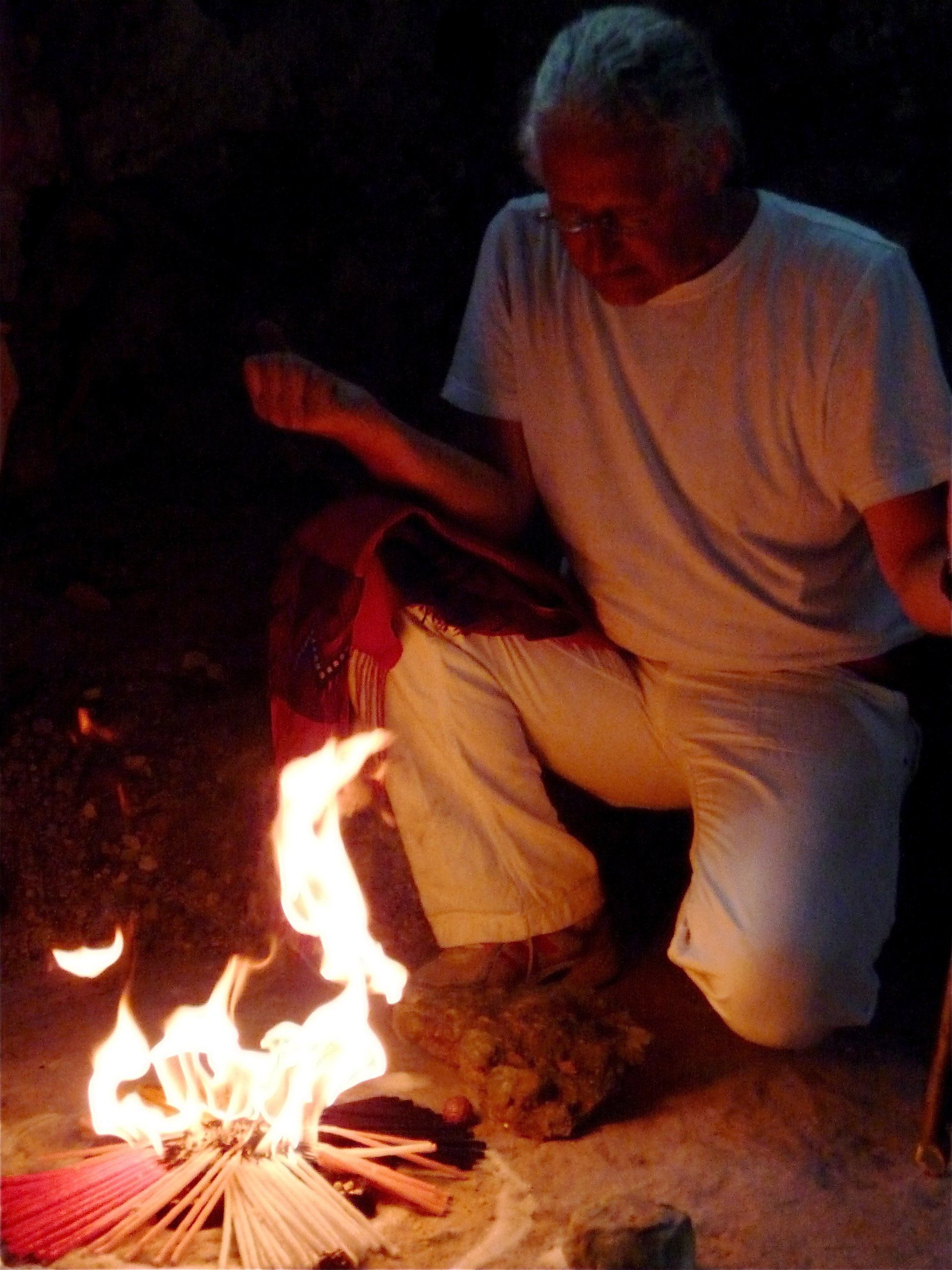 Ein Mann in einem weißen Hemd kniet vor einem Feuer