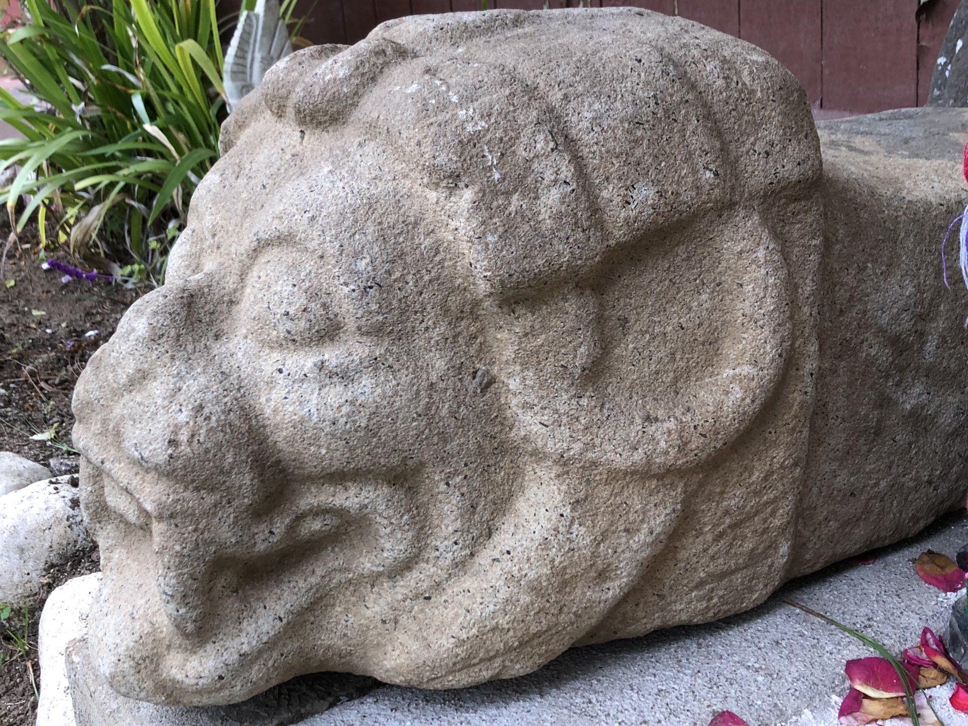 Eine große Steinstatue eines Löwenkopfes sitzt auf einem Gehweg.