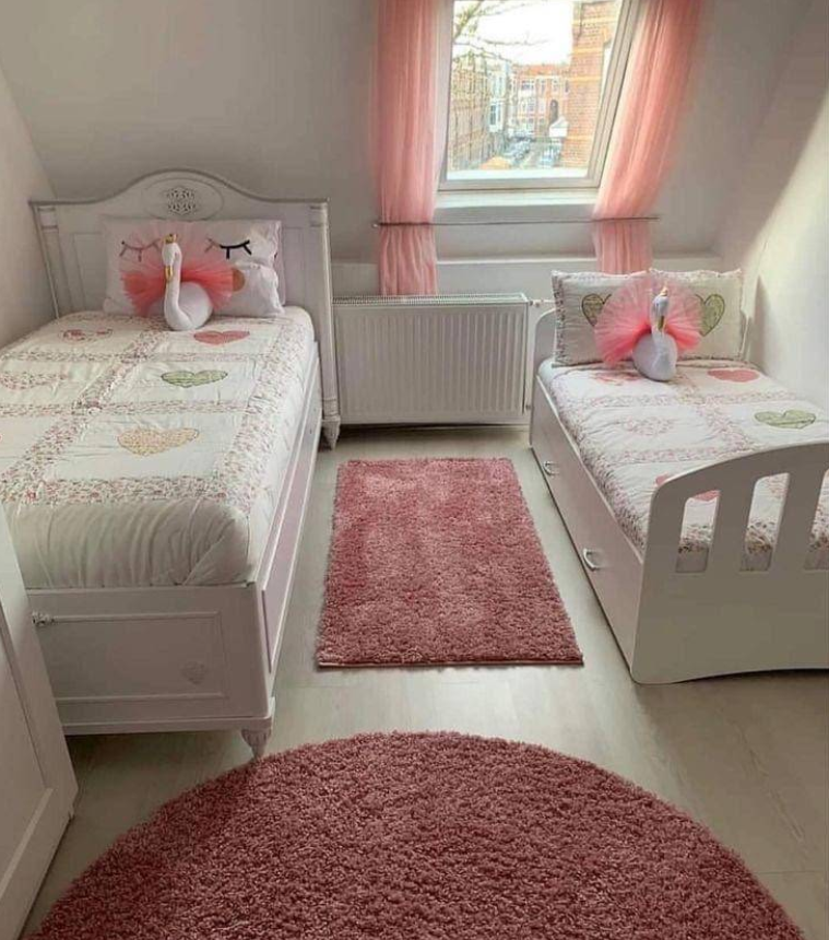 Two white beds in a pink-themed room with matching bedding, curtains, and rugs.