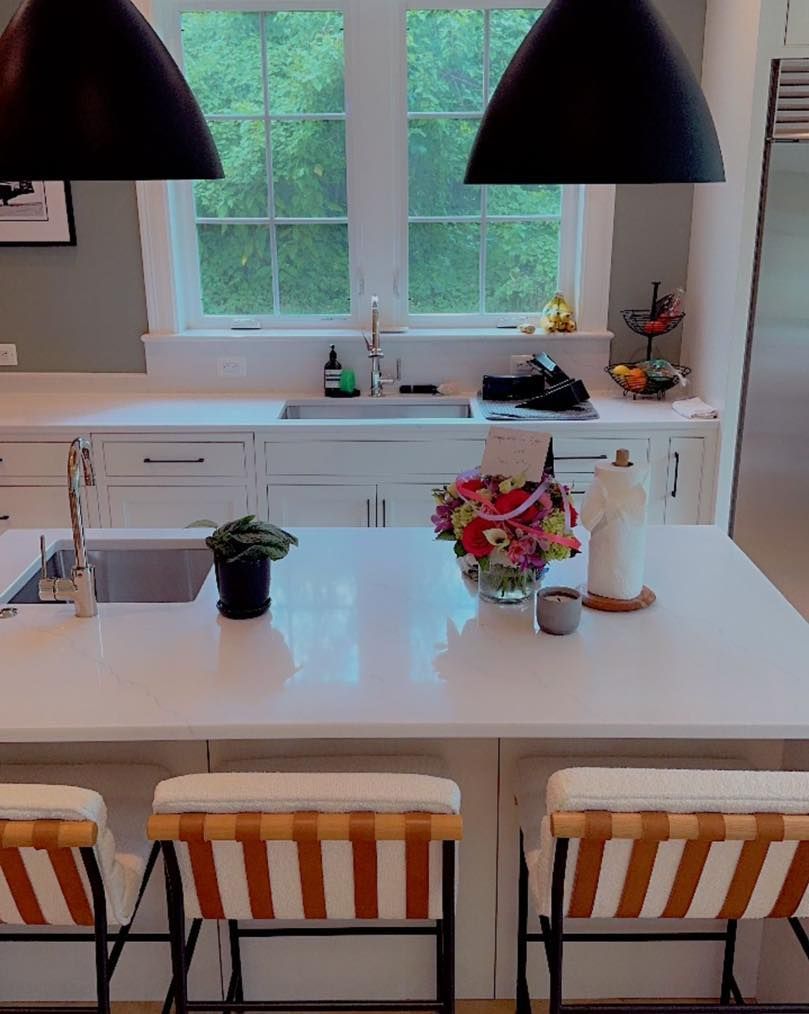 Kitchen with white countertops, black pendant lights, a central island with stools, and a window overlooking greenery.
