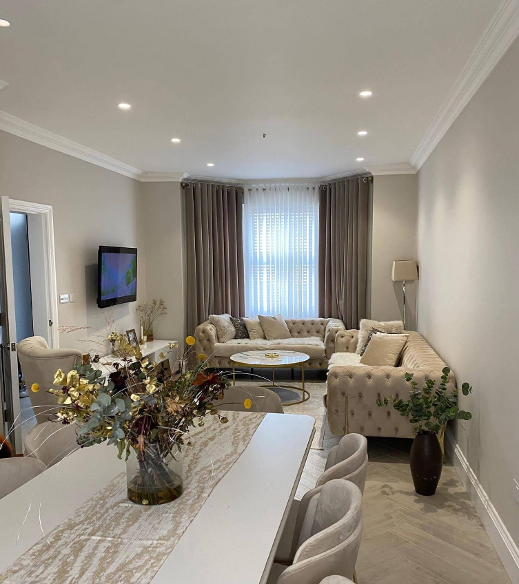 Elegant living room with beige furniture, large curtains, and a long dining table.