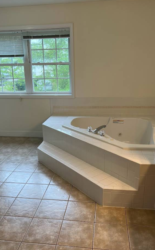 Bathroom with a white jacuzzi tub on a tile platform near a window.