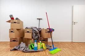 Cleaning supplies and cardboard boxes on a wooden floor in a bare room, with a broom and mop leaning nearby