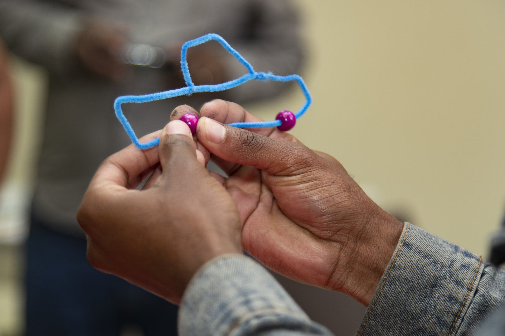 An image of hands holding a vehicle made with blue pipe cleaners