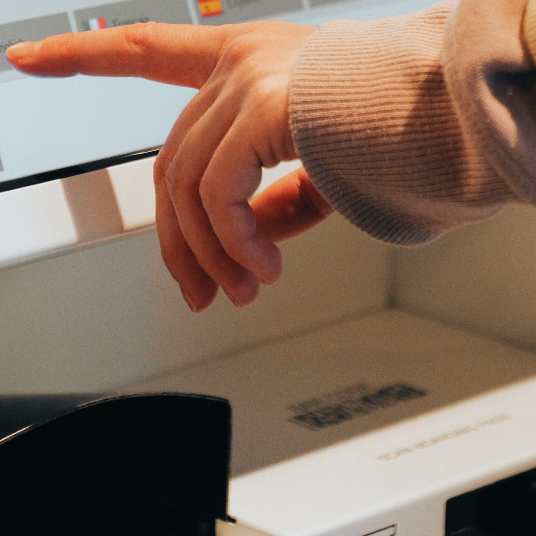 A hand about to press a button at a kiosk
