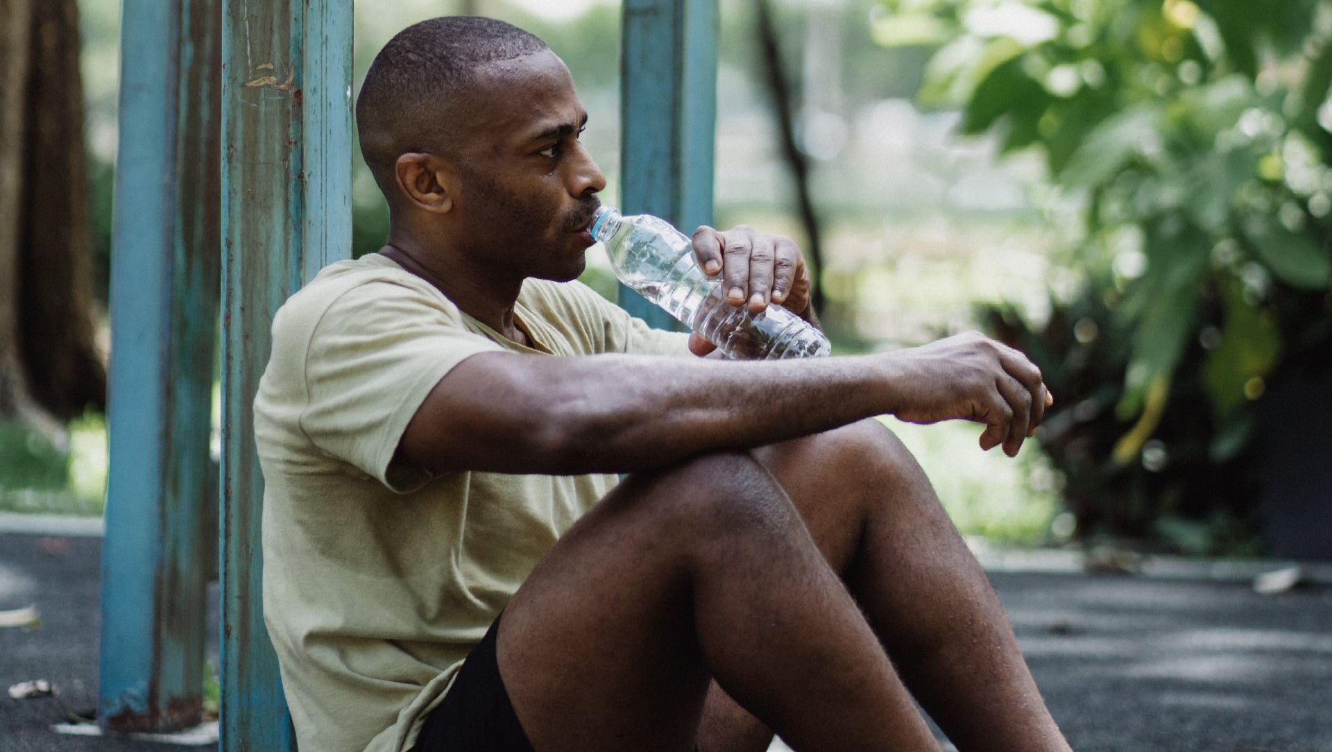 A young man in running gear sitting on the pavement and drinking from a plastic water bottle
