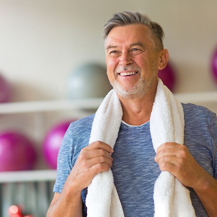 A man with a towel around his neck is smiling in a gym.