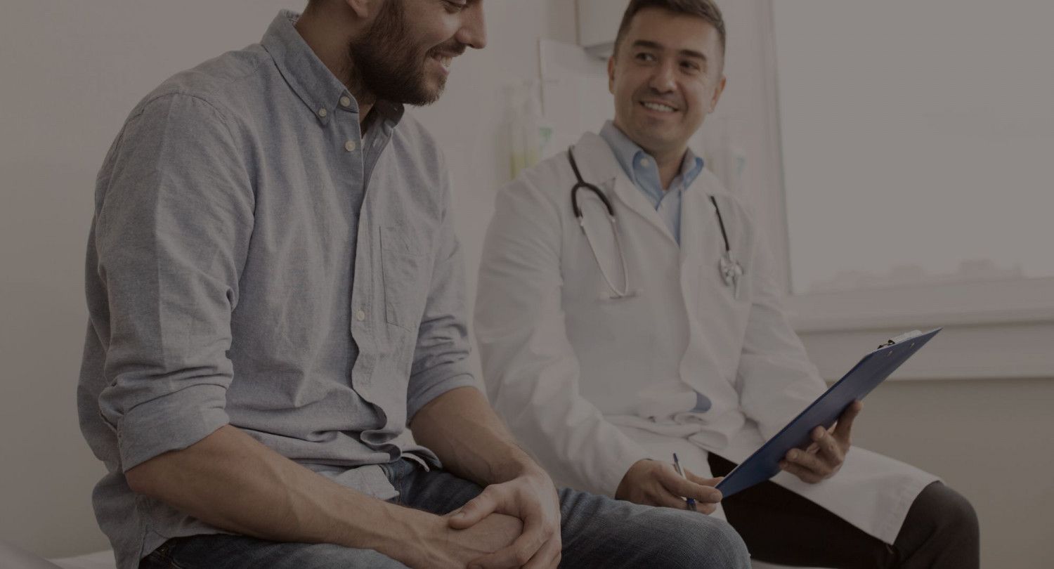 A man is sitting on a bed talking to a doctor.