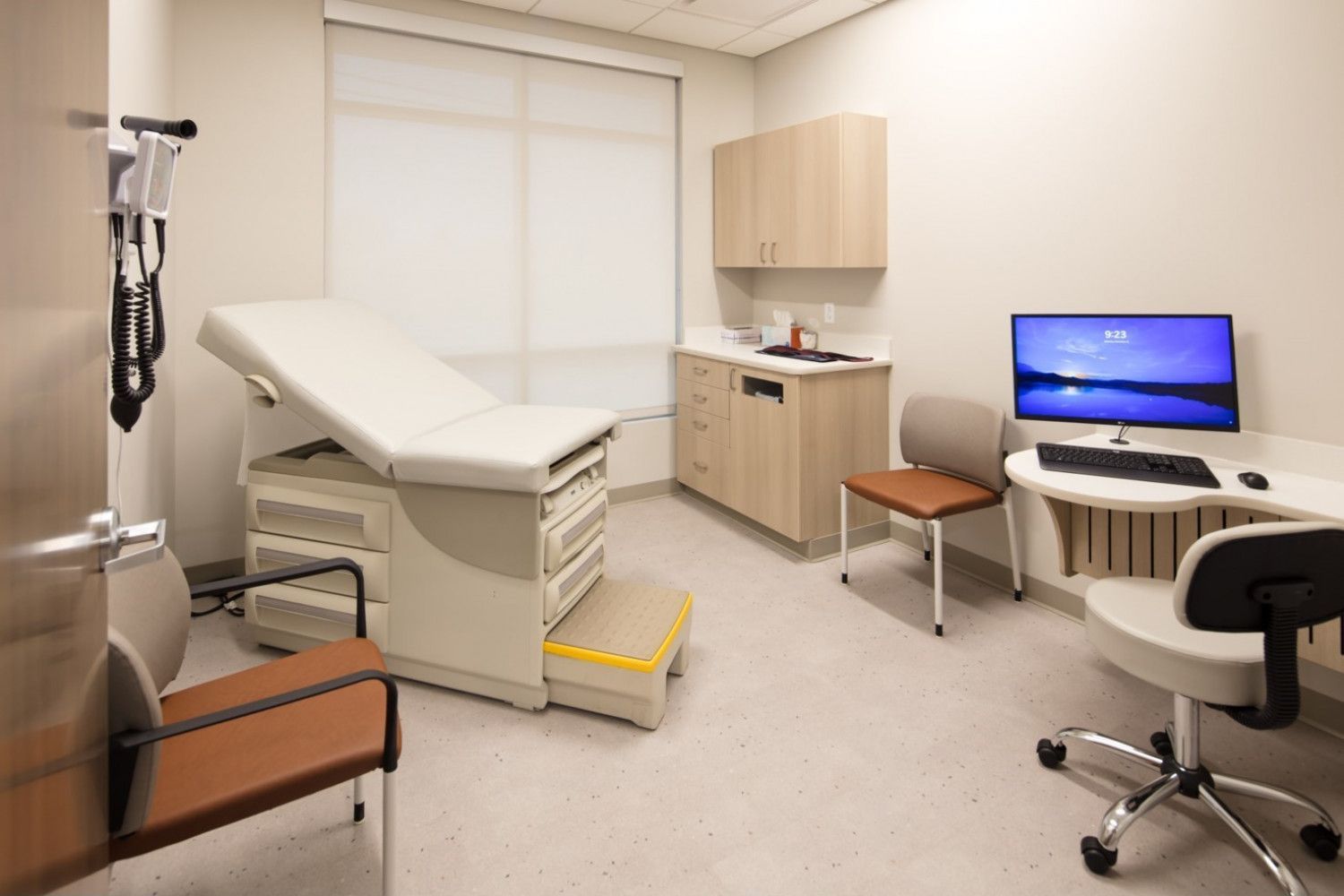 A doctor 's office with a couch , chair , desk and computer.