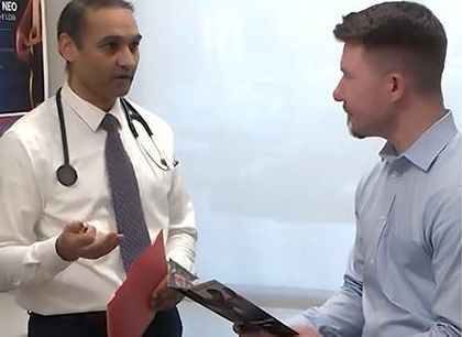 Doctor speaking with a man while holding a red folder in a bright office.