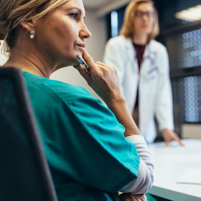 A woman in a green scrub is sitting at a table with a pen in her hand.
