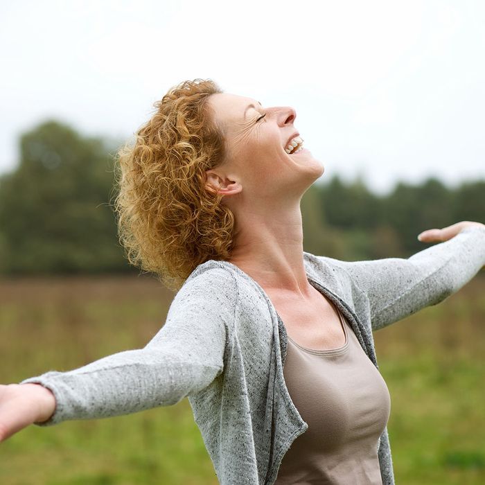A woman is laughing with her arms outstretched in a field