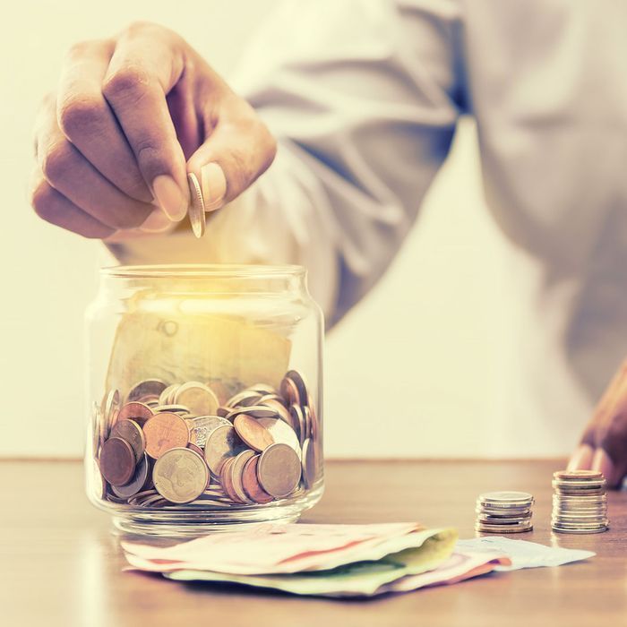 A person is putting coins into a jar on a table.