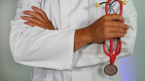 A doctor is holding a red stethoscope with his arms crossed.