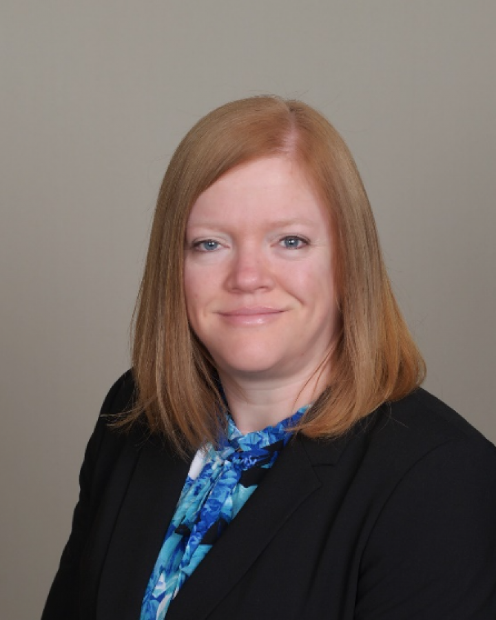 A woman wearing a black jacket and a blue shirt is smiling for the camera.