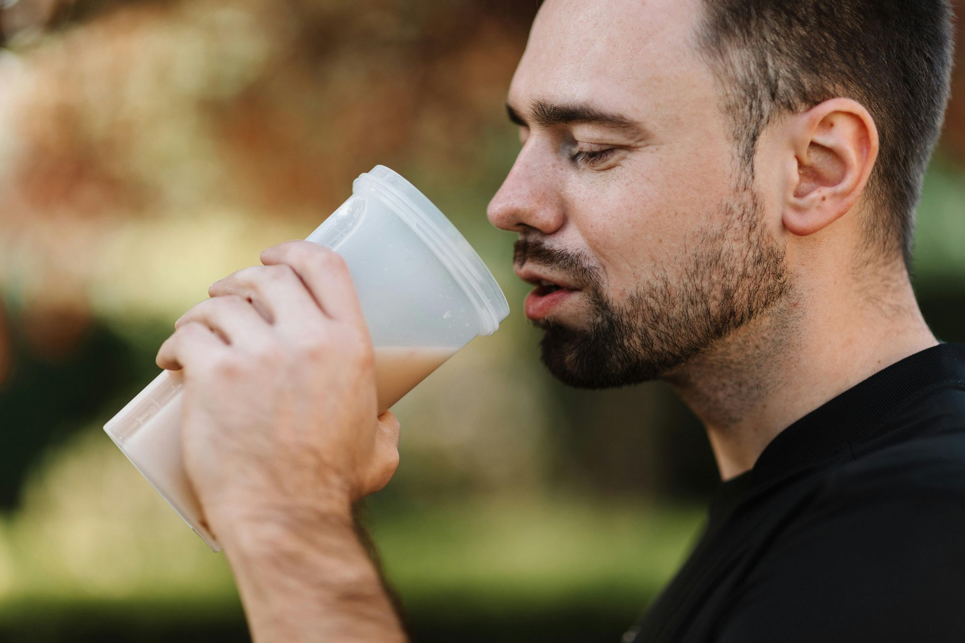 A man is drinking a protein shake from a shaker.