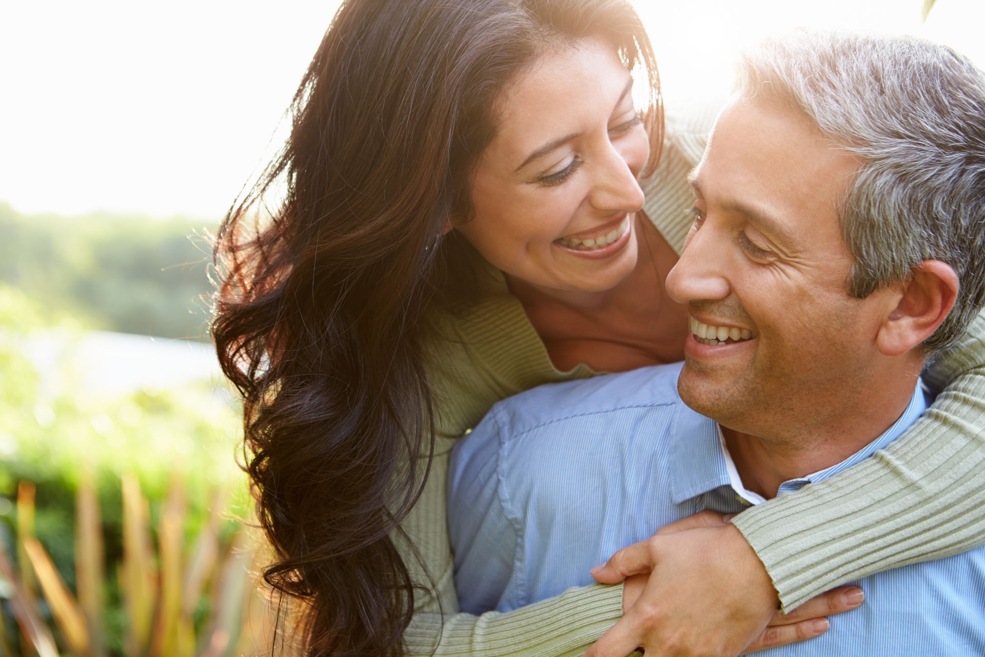 Two people smiling and embracing outdoors in warm sunlight.
