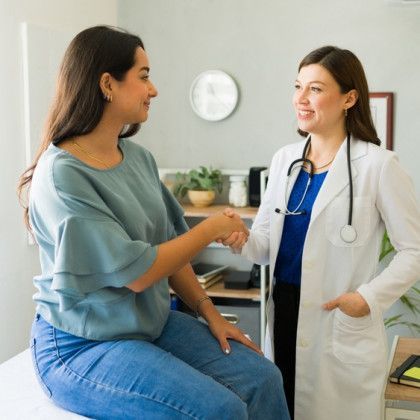 A doctor is shaking hands with a patient who is sitting on a bed.