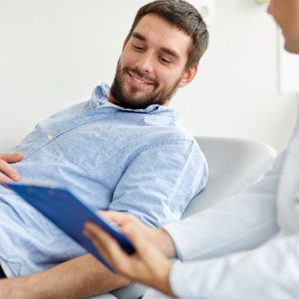 A man is sitting in a chair talking to a doctor while holding a clipboard.