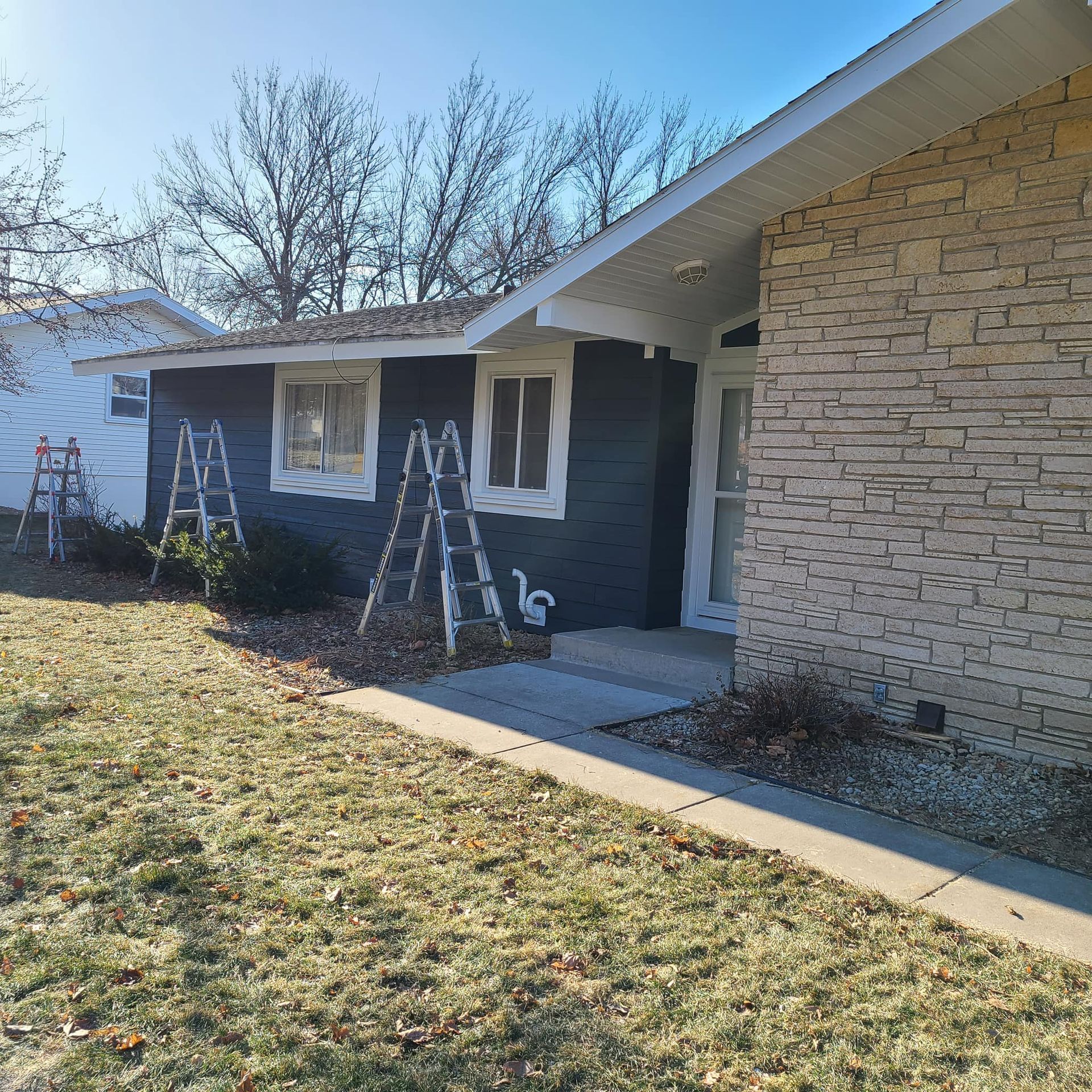 Exterior of a house being painted blue. Ladders are set up, with unpainted windows.