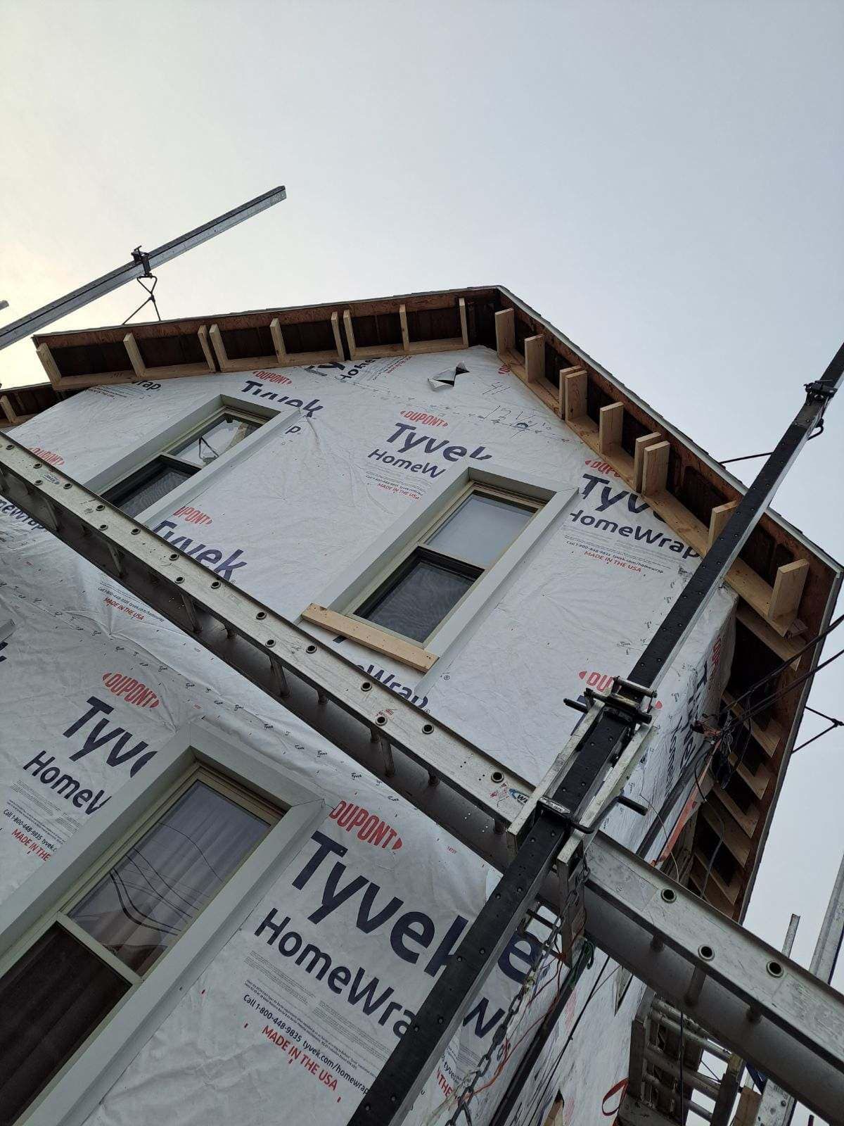 A house under construction, wrapped in Tyvek HomeWrap, with scaffolding and windows visible.