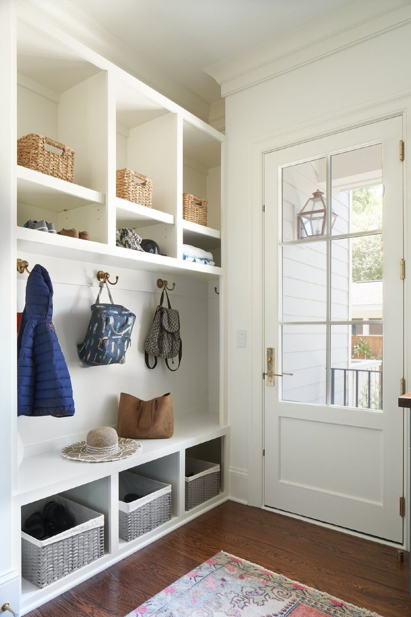 A mud room with a bench , shelves , baskets and a door.