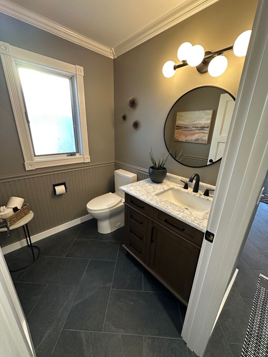 A bathroom with a toilet , sink , mirror and window.