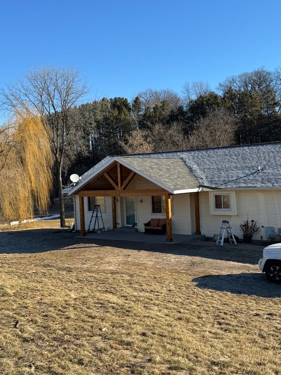 Tan house with a wooden porch, blue sky. Sparse trees, dry grass.