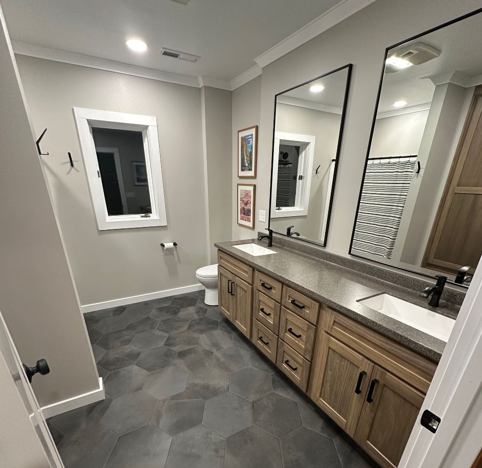 A bathroom with two sinks , two mirrors and a toilet.