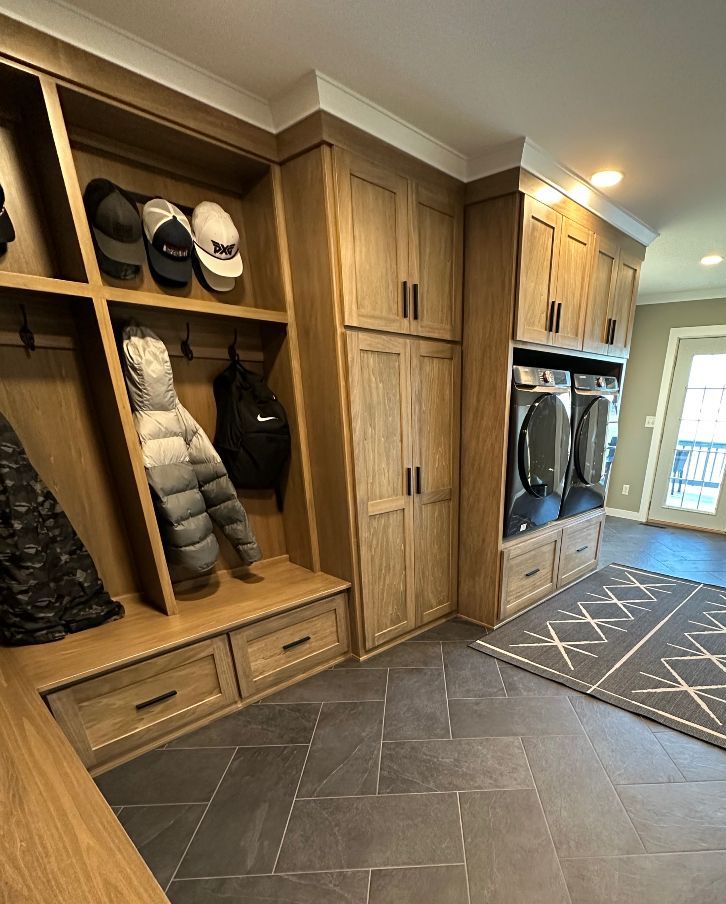 A mud room with wooden cabinets , a washer and dryer , and a rug.