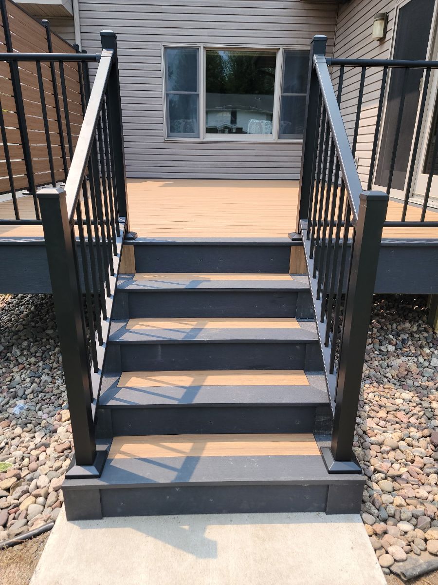 A set of stairs leading up to a deck with a black railing.