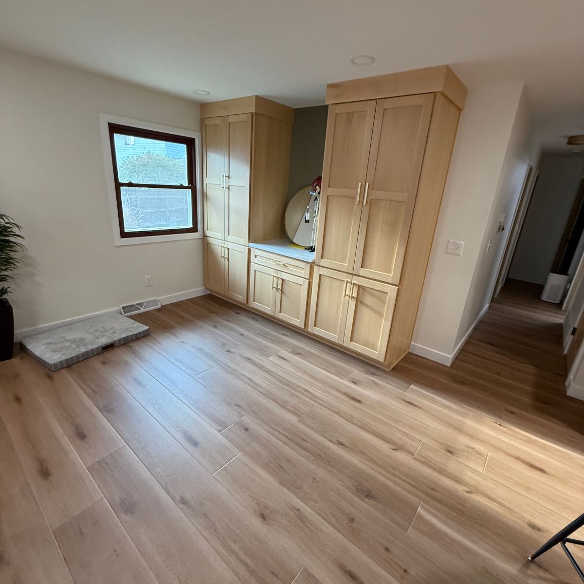 Light-colored wooden built-in cabinetry with a countertop, placed against a wall next to a window in a room with wood floors.