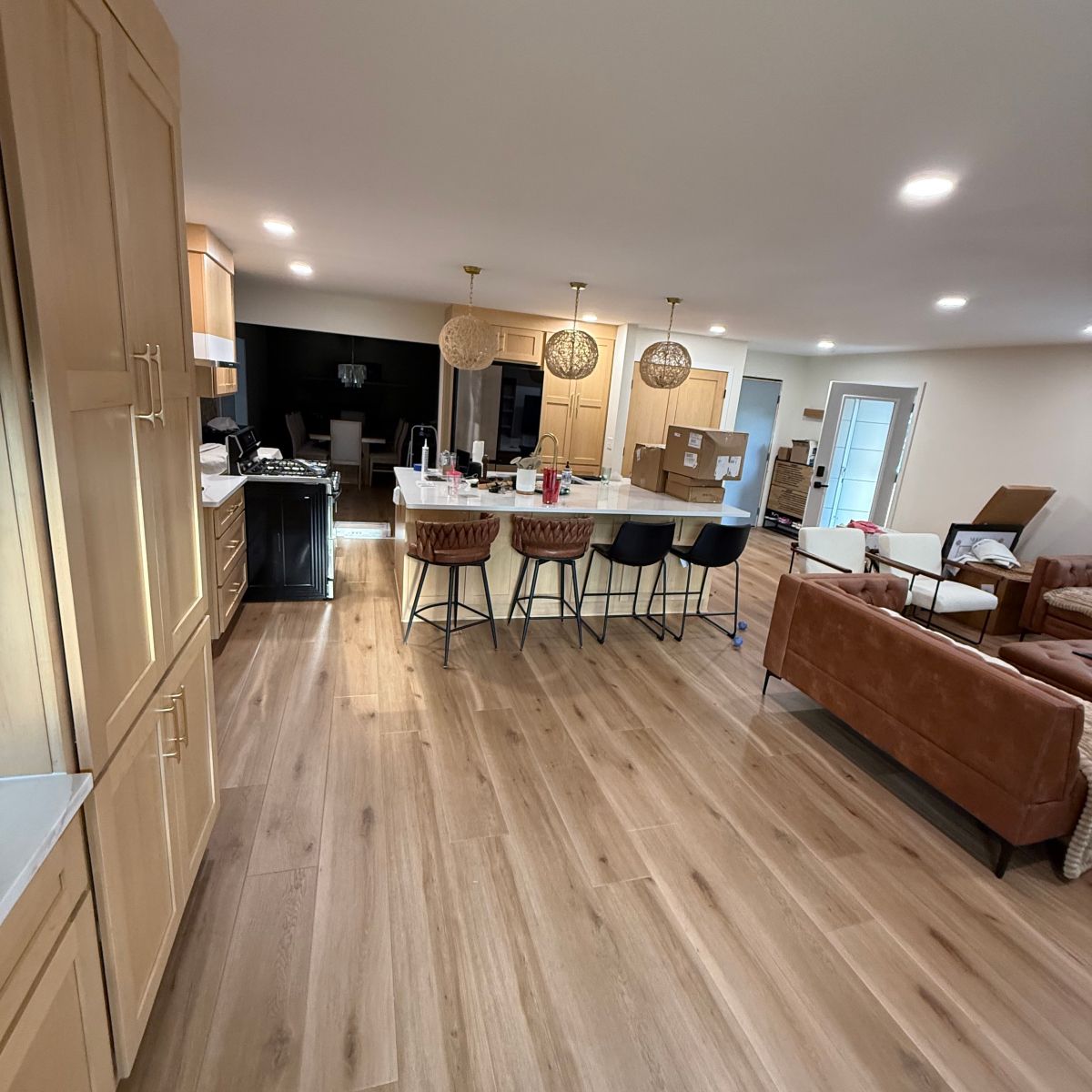 A bright open-concept kitchen and living area featuring light wood cabinets, a central island with bar stools, and sofa.