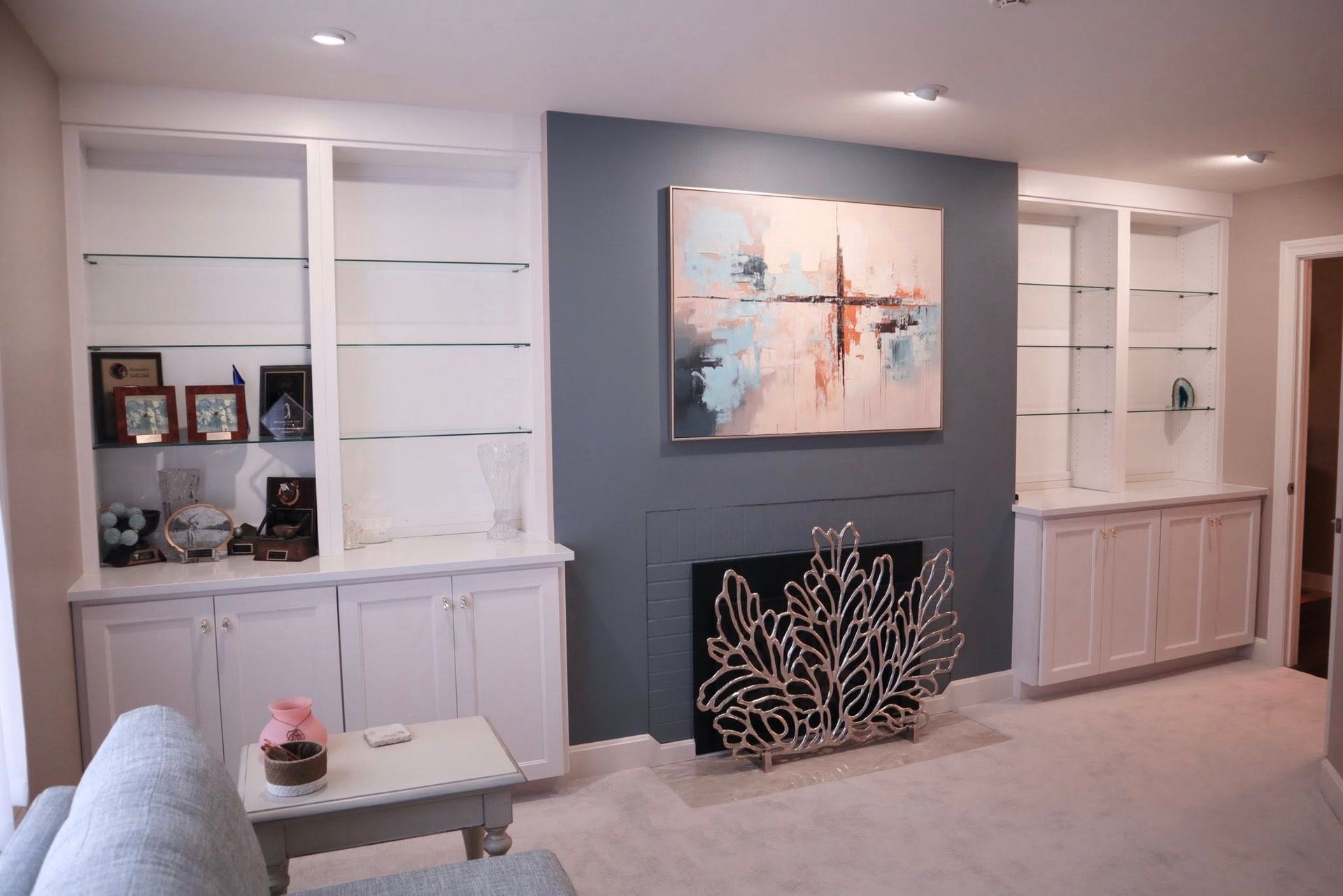 A living room features a fireplace with a blue accent wall, abstract art, and white built-in shelves on either side.